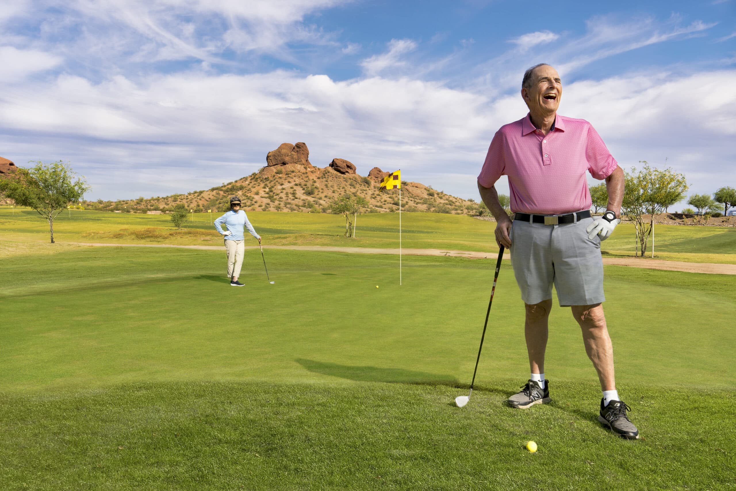 Two happy older adults stand on a golf course.